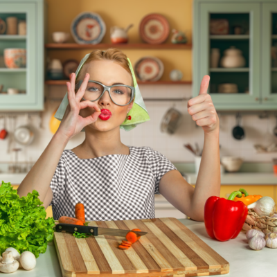 Mulher numa cozinha a fazer gestos positivos com as mãos relativamente à comida caseira que recebeu em casa